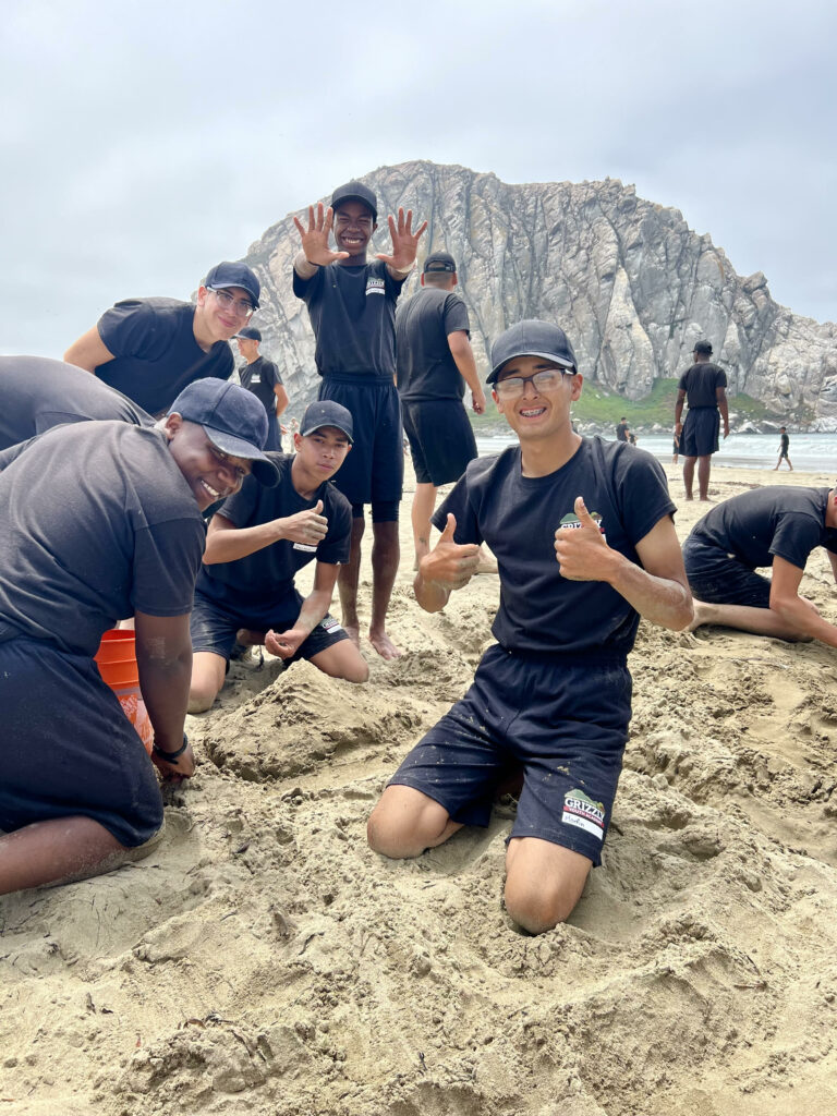 A group of students at the beach, one student giving a thumbs up to the camera.