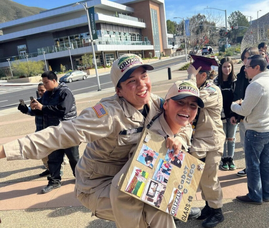 Two graduates, one on the other's back, celebrating.