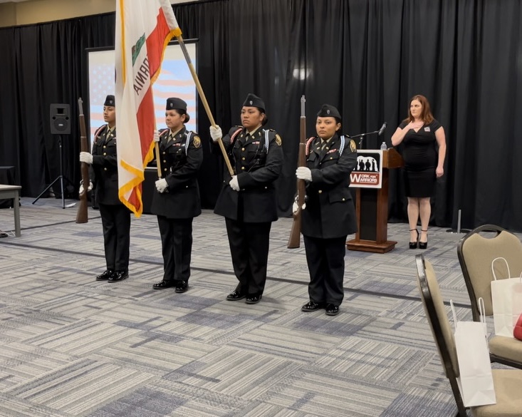 Four students in uniform, one carrying the California state flag, the other three at attention with rifles.